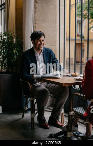 Calm relaxed young couple sitting at table next to window and drinking coffee and talking while having breakfast in cafe Stock Photo