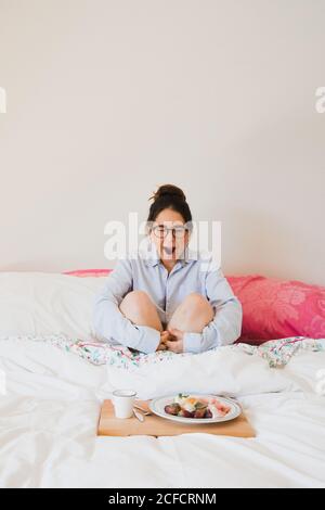 Portrait of Woman yawning while sitting on bed in front of a tray with healthy food Stock Photo