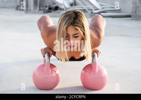 Blond haired stylish Woman during performing push ups on pink big dumbbells on roof of building Stock Photo