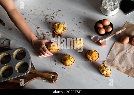 From above crop person hand holding a homemade cupcakes on wooden table with arranged eggs Stock Photo