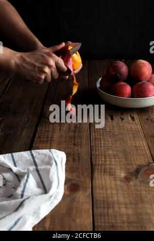 Tasty ripe peaches in plate and hands peeling peach Stock Photo