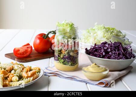 Yummy pasta with fresh vegetables and sauce placed inside jar on white table Stock Photo