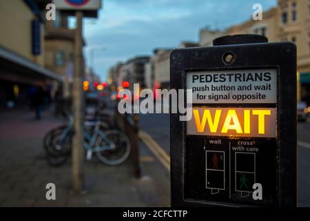 Modern instruction panel for traffic light with glowing wait sign on blurred background of evening street in Brighton, England Stock Photo