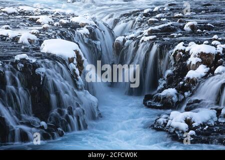 Amazing Nordic scenery of frozen waterfalls and river flowing through rough volcanic terrain covered with snow in Iceland Stock Photo