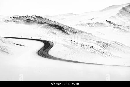Curvy asphalt road going through snowy white hills on winter day in Iceland