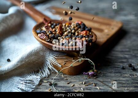 Spice fragrant mix of fresh spices and dried berries on wooden spoon on linen on wooden stand at table Stock Photo
