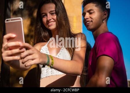 Charming young lady taking selfie on phone with content ethnic guy Stock Photo