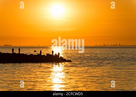 Sun sets over the Copenhagen skyline, anglers stand on a pier in the foreground Stock Photo