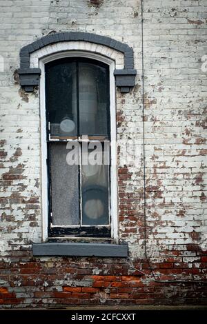 Old arched window set into a weathered brick wall with peeling paint and faded colors reflecting urban decay Stock Photo