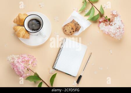 Morning cup of coffee, empty notebook, snacks and hydrangea flowers. Top view, flat lay. Stock Photo