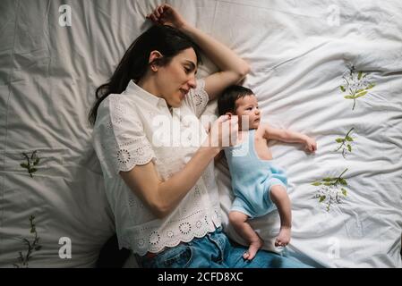 Beautiful adult Woman gently touching sweet baby while lying on comfortable bed together Stock Photo