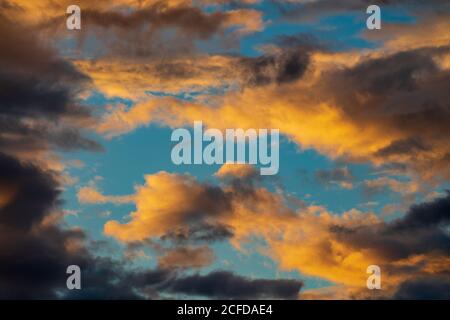 Dramatic fluffy clouds illuminated by disappearing rays at sunset, dark thunderclouds floating across blue sky to weather change Stock Photo