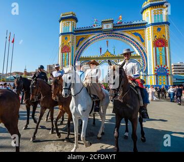 Riders on decorated horses in traditional dress in front of the entrance gate, Feria de Abril, Seville, Andalusia, Spain Stock Photo