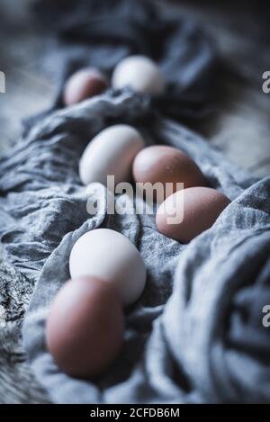 Bunch of chicken eggs lying in tablecloth on rustic wooden table. Stock Photo