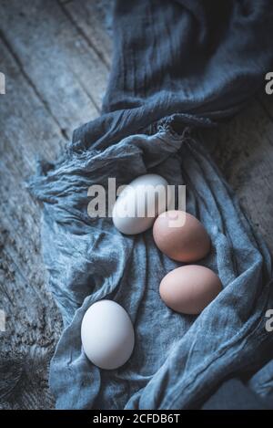 Bunch of chicken eggs lying in tablecloth on rustic wooden table. Stock Photo