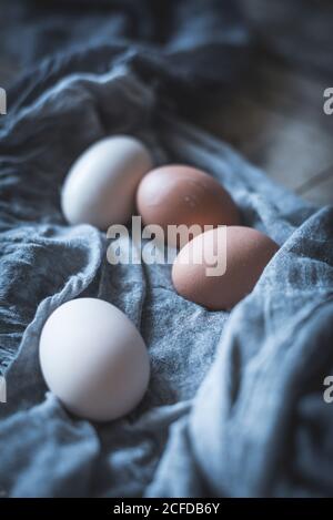 Bunch of chicken eggs lying in tablecloth on rustic wooden table. Stock Photo