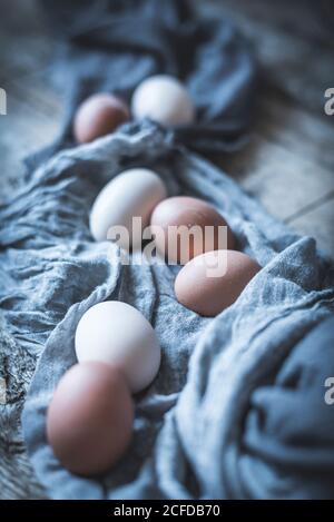 Bunch of chicken eggs lying in tablecloth on rustic wooden table. Stock Photo