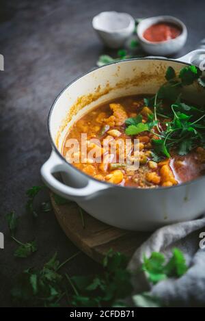 Top view of bowl of delicious vegan chickpea curry with herbs placed near fabric napkin on gray tabletop Stock Photo
