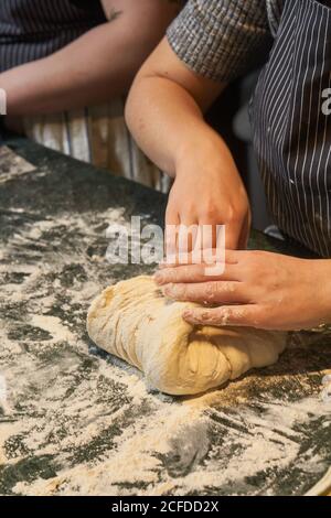 From above of faceless female hands kneading bunch of fresh dough at table in bakery Stock Photo