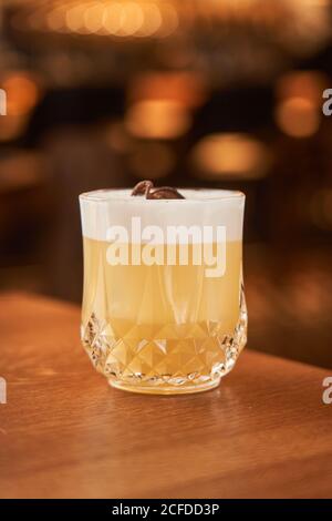 Glass of classic alcohol cocktail Whiskey Sour with lemon juice and egg white placed on wooden counter Stock Photo