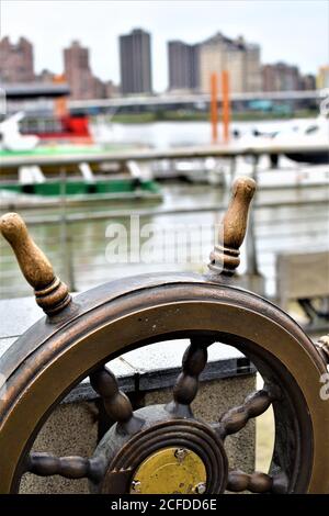 A bronze metal steering wheel on a riverside park Stock Photo