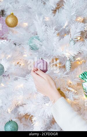 faceless female hanging Christmas decorations on artificial white fir tree at home Stock Photo