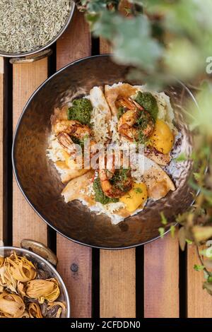 From above tasty fresh fried eggs with shrimps covered by herbs in pan on wooden table in garden Stock Photo