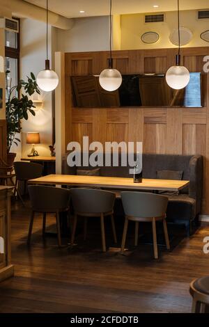 Dark bottle on yellow able surrounded by chairs in elegant interior of stylish restaurant with warm light of fashion round lamp Stock Photo