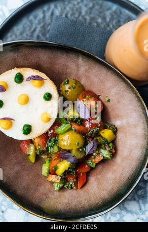 From above red ripe sliced tomatoes onion pepper herbs in ceramic plate on table in restaurant Stock Photo
