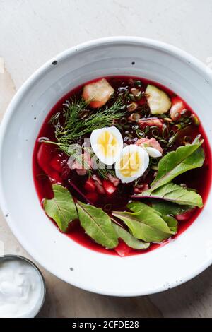 From above palatable red beetroot soup with boiled eggs and herbs in white plate on table Stock Photo