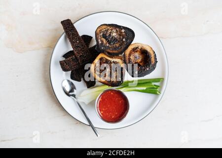 Top view of smoked rounded slices of eggplant on white plate with red sauce green onion and fried croutons of rye bread in restaurant Stock Photo