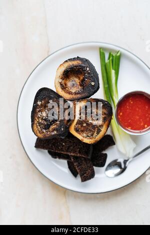 Top view of smoked rounded slices of eggplant on white plate with red sauce green onion and fried croutons of rye bread in restaurant Stock Photo