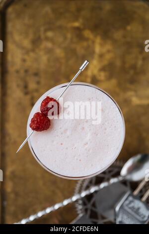 Top view of colorful red alcohol cocktail in stylish glass on table with bar spoon and strainer in restaurant Stock Photo