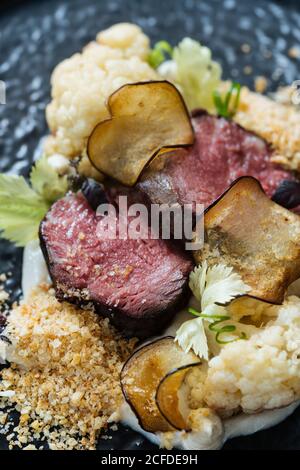 Back plate with roast beef slices on creamy sauce with cauliflower and fried chips having dinner with glass of red wine Stock Photo