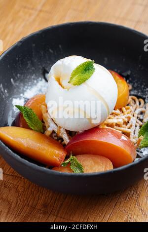 From above of fresh slices of mango with creamy ice cream and sweet spaghetti decorated with mint in stylish black bowl Stock Photo