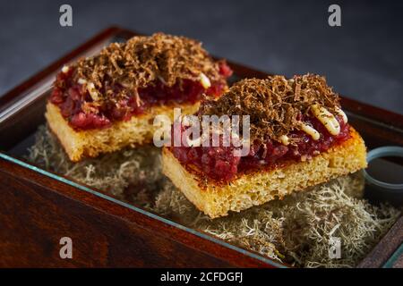 Sweet sponge cake with berry marmalade and chocolate curls placed on box with dry moss Stock Photo