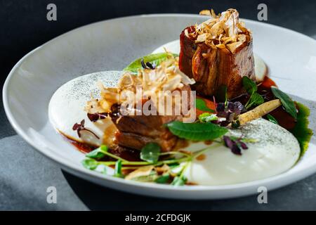 Closeup pieces of roasted meat with truffles and fresh herbs served on plate in cafe Stock Photo