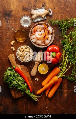 Top view of various ripe vegetables and herbs placed near juicer and boiled shrimps on wooden table in kitchen Stock Photo