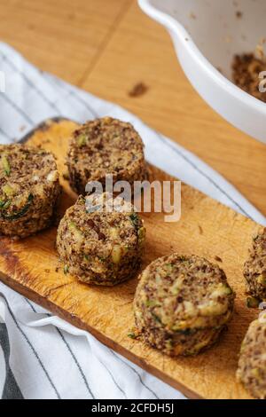 Healthy vegan round raw cutlets made from lentil and zucchini on wooden cutting board placed on wooden table with white striped cloth Stock Photo