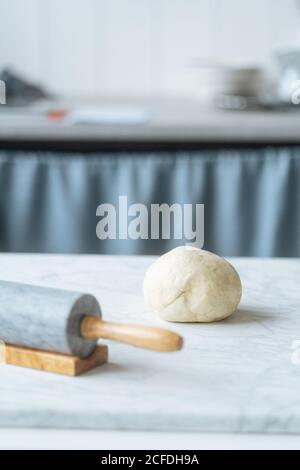Fresh kneaded dough on table with rolling pin ready for preparing pasty in light kitchen Stock Photo