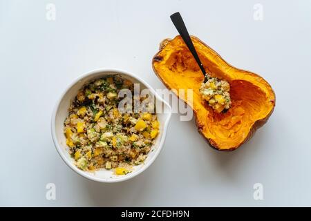 Top view of bowl with vegan mixed filling with quinoa and vegetables and half of baked orange pumpkin with spoon on white background Stock Photo