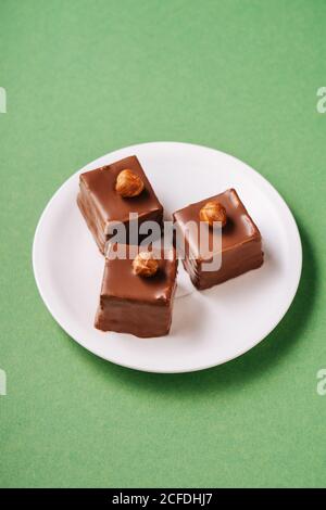 From above pieces of yummy pastry with chocolate icing and hazelnuts placed on plate on green background Stock Photo
