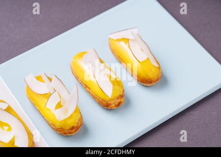 Closeup tasty eclairs with banana icing and pieces of coconut placed on blue board Stock Photo