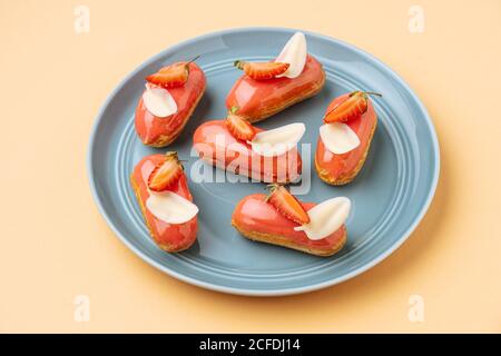 From above delicious eclairs with strawberry icing and white chocolate leaves placed on beige background Stock Photo
