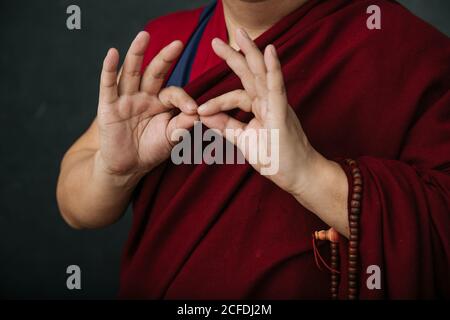 Closeup of hands of crop praying Tibetan monk in traditional red robe with mudra symbolic hands gesture Stock Photo