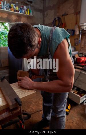Side view of workman using wooden mallet while working with wooden plank in small workshop Stock Photo