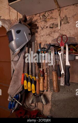 Set of work tools and protective clothes for welding and soldering hanging on old flake wall of workshop Stock Photo