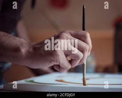 Closeup hand of anonymous artist using paintbrush and green paint to draw picture on canvas in studio