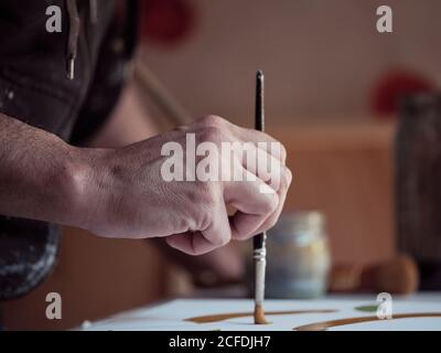 Closeup hand of anonymous artist using paintbrush and green paint to draw picture on canvas in studio