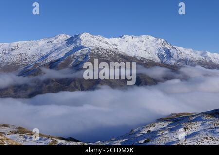 Thick fog flows in the valley between half snow-covered mountains Stock Photo